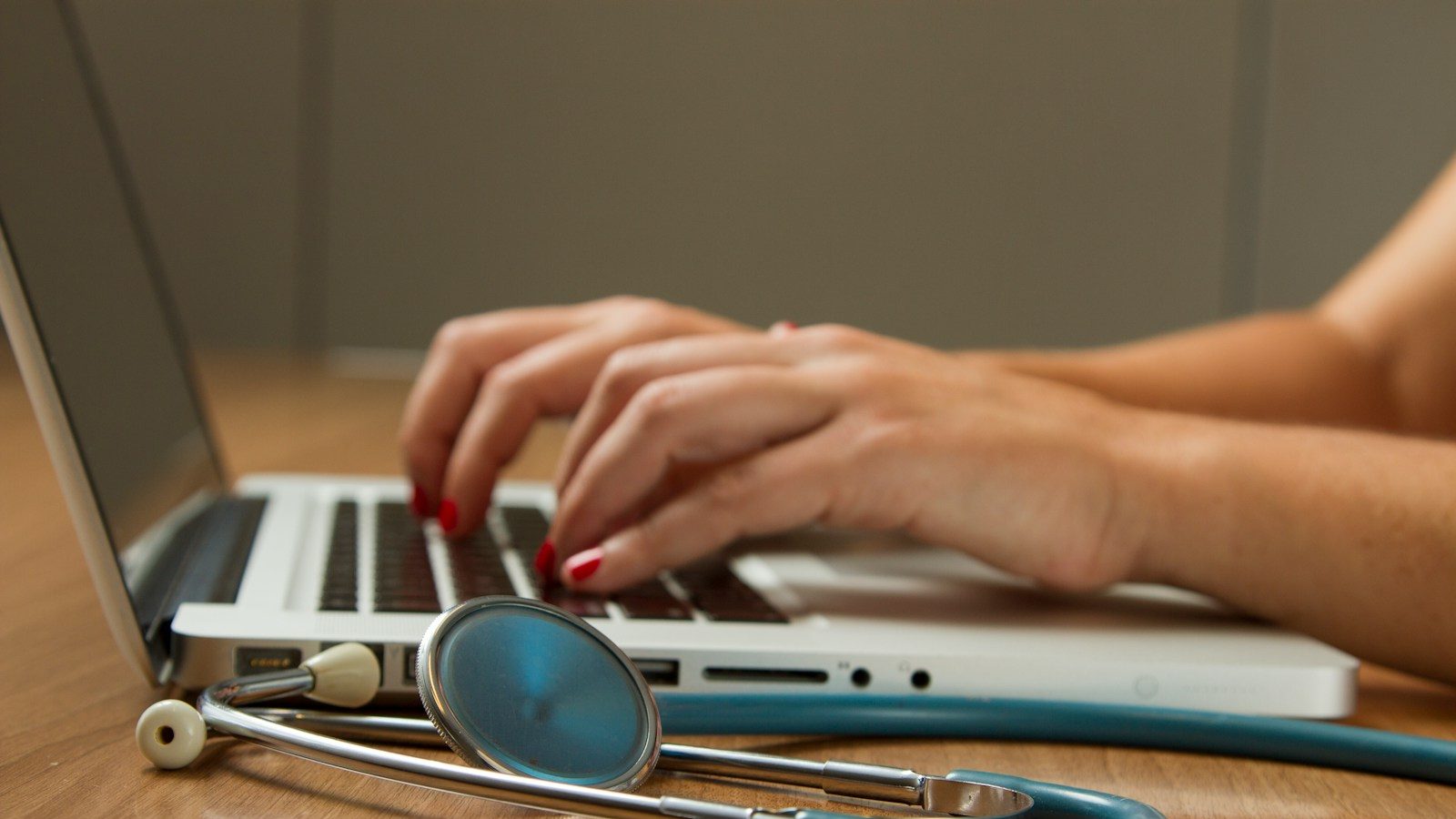 person sitting while using laptop computer and green stethoscope near